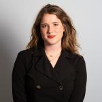 white girl with brown hair standing in front of blank wall wearing a black blazer