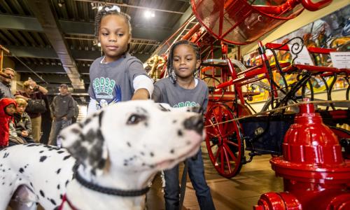 two little girls with a white, spotted dog (dalmation) at a fire station museum