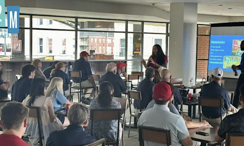 people sitting and listening while two people stand at the front of the room talking