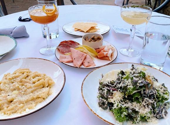 plates of pasta, salad, charcuterie, and cocktails on a white tablecloth on a patio