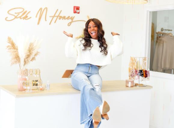 woman sitting on counter of brightly lit boutique, she's laughing and her hands are in the air