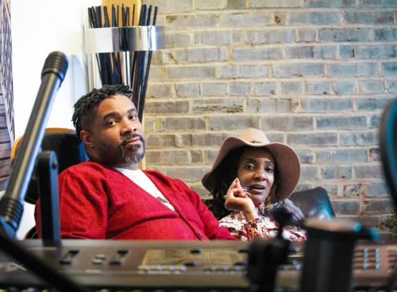 man in red jacket and woman in hat sitting in music studio