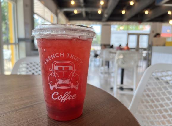 dark pink colored iced tea in a plastic cup in the foreground, background is coffee shop interior with white chairs and lots of windows