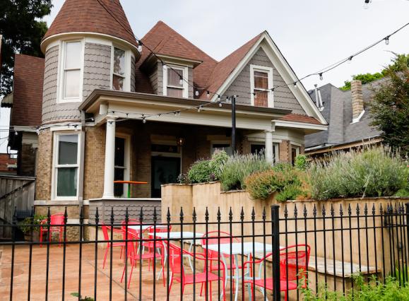 gray house with turrets that's been turned into a restaurant, shrubs all around, patio with red furniture out front