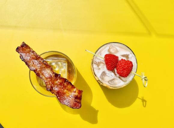 cocktail with bacon and cocktail with raspberries sitting on a yellow table