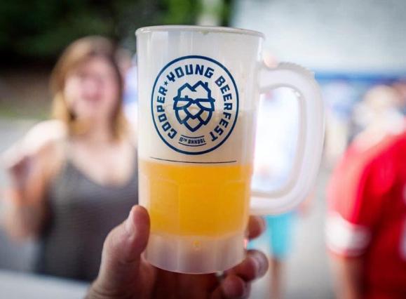 plastic beer mug with handle and logo, half filled with beer, held up in front of out of focus crowd