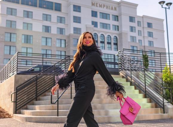 woman in black jumpsuit walking with pink purse in front of multi-story memphis hotel