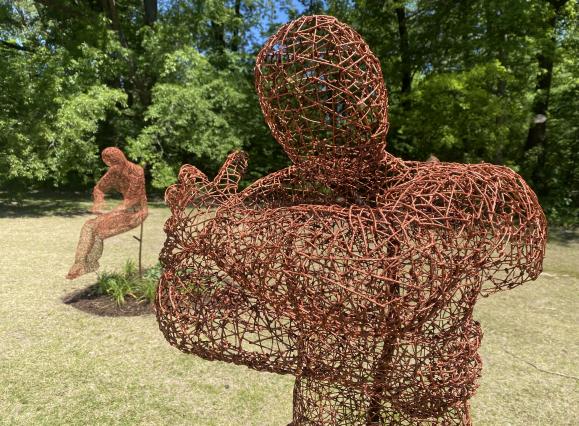 two metal wire silhouettes of a man with crossed arms and other looking down