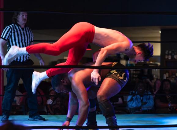 wrestler flies over the back of another wrestler who is bent over
