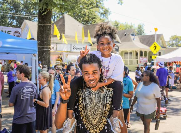 man with young girl on shoulders both hold up peace signs at Cooper young festival
