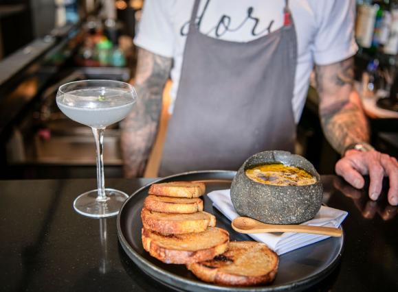 man stands behind bar with appetizer and mocktail sitting on bar