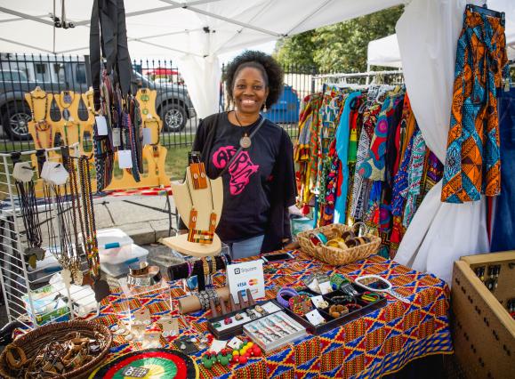 woman poses behind table of her vendor shop of jewelry and clothes