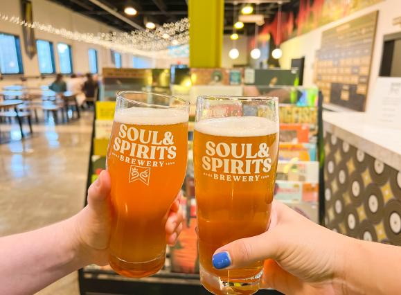 two beers being held in cheers with brewery name on them