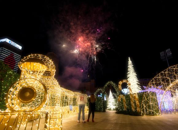 elaborate light display of a train, Christmas Tree, and more with two people watching fireworks in the sky