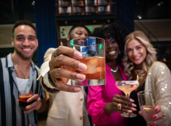 four friends hold up cocktails and smile for photo