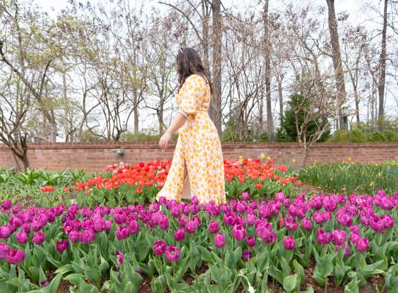 woman in flowy yellow dress walking through purple and orange flower field
