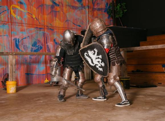 two people in knight armor battle with swords and shields