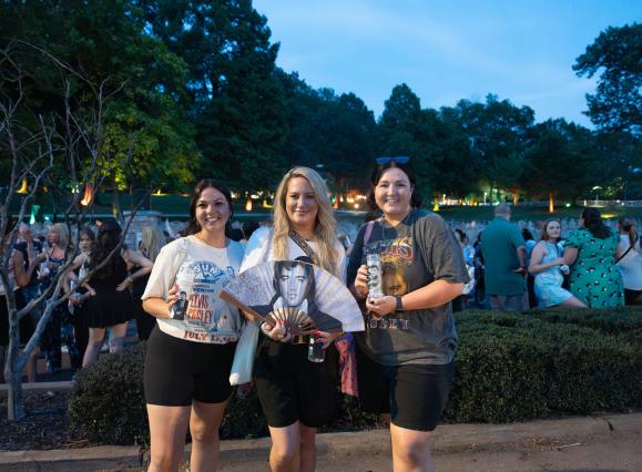 three women pose for photo with elvis memorabilia at candlelight vigil at Graceland