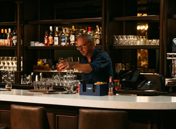 BARTENDER pours a drink behind bar at The Dame