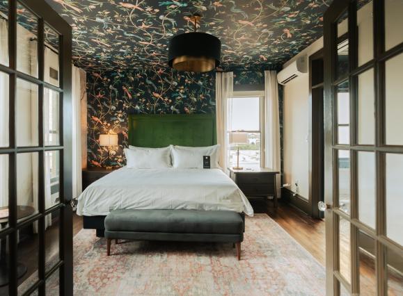 doors open into suite hotel room of Hotel Pontotoc with bed, wallpaper on back wall and ceiling