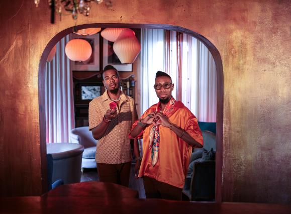 two African American men standing next to each other, one making a heart symbol with his hands and one holding out a rose