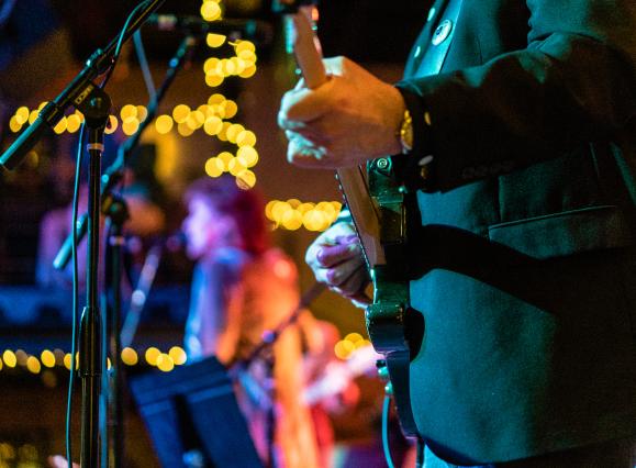 close up of man playing guitar with holiday lights in background