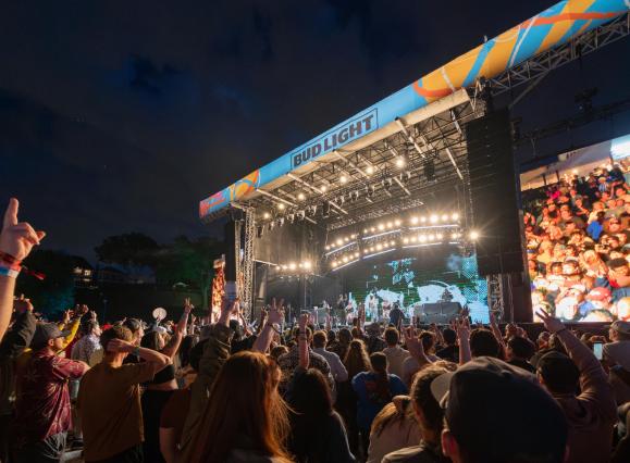 Crowd watching a performer on stage at night at RiverBeat Music Festival.