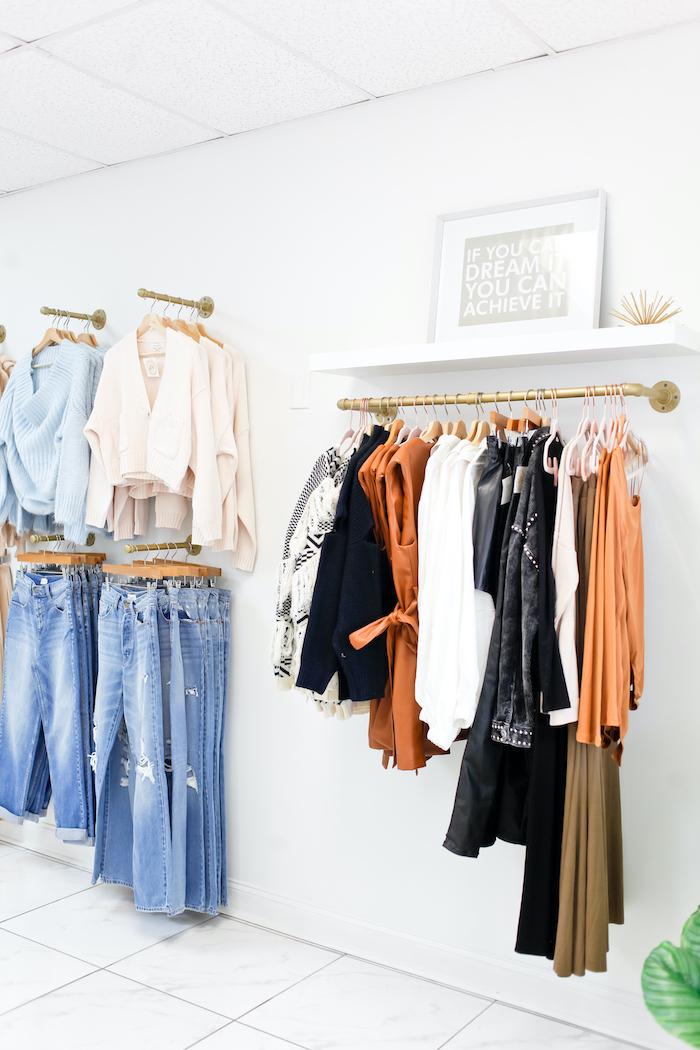 jeans, sweaters, and dresses hung up in a boutique against a white wall