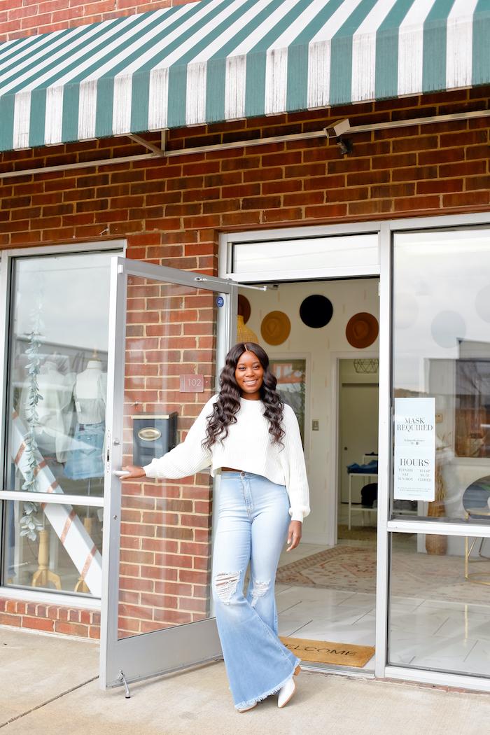 woman standing holding door open to clothing boutique