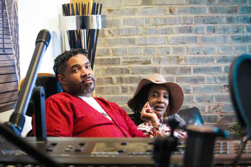 man in red jacket and woman in hat sitting in music studio