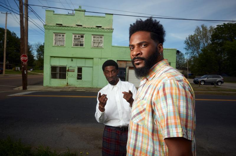 two men standing in front of historic green buildling