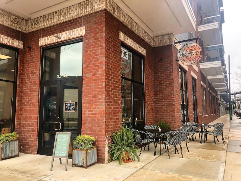 exterior of cafe, red brick with large windows, a few planters and two tables for patio seating