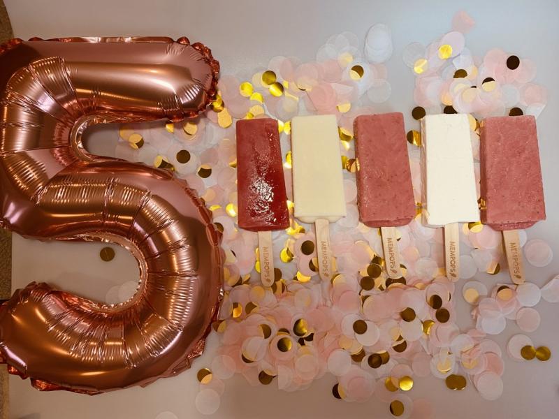 shiny balloon of the number 5 and pink and white popsicles with confetti all around