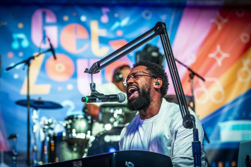 pj morton singing on stage with colorful Get Loud poster in background
