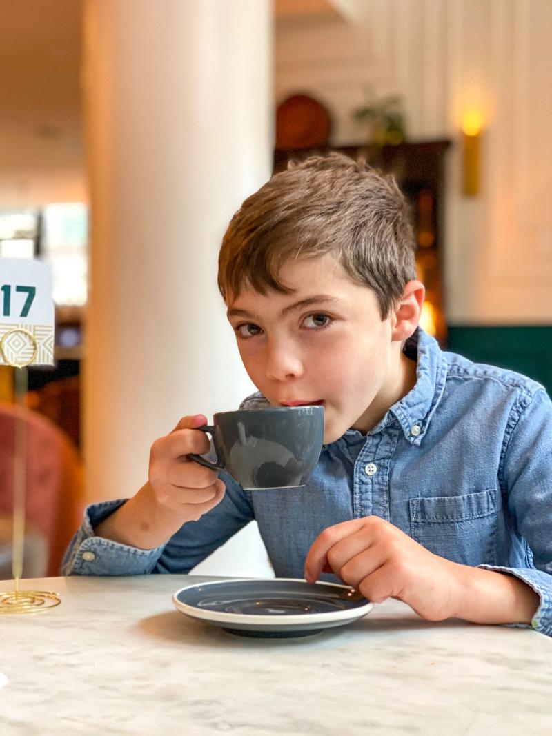 school aged boy sipping from hot chocolate cup at ARRIVE hotel
