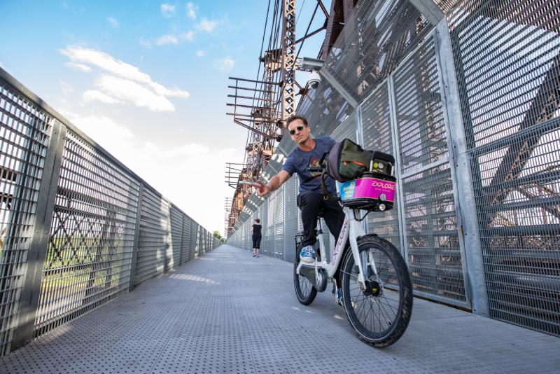 man on bike riding across Big River Crossing and waving