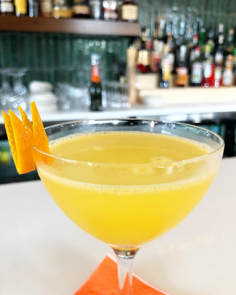 bright yellow cocktail with orange garnish with bar background