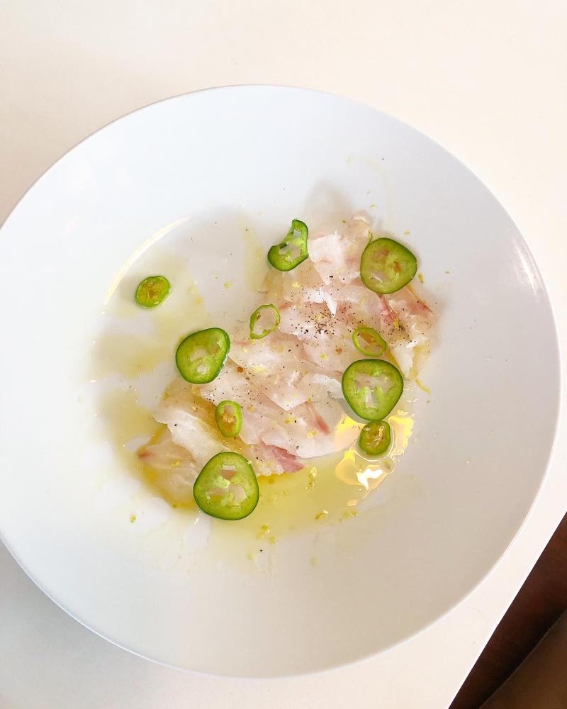 light pink raw fish crudo drizzled in oil with thin slices of jalapeño