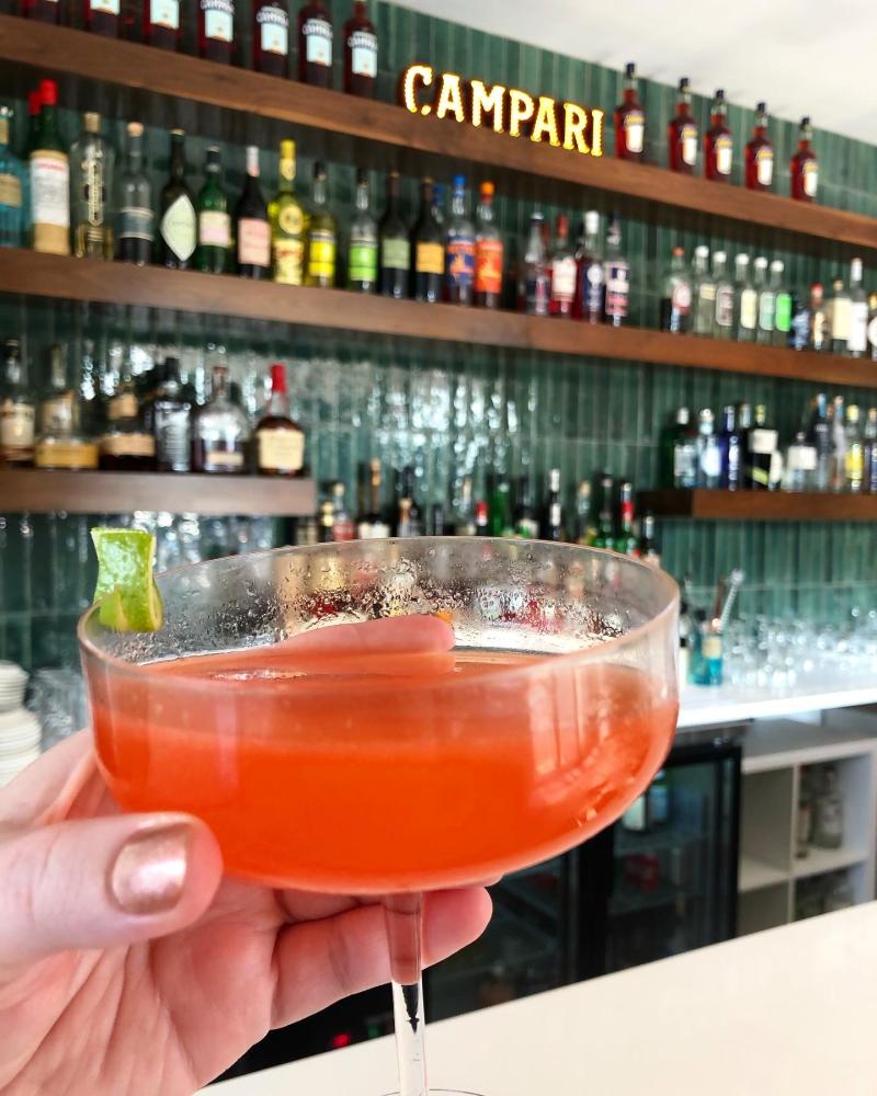 bright red cocktail held up in front of upscale bar
