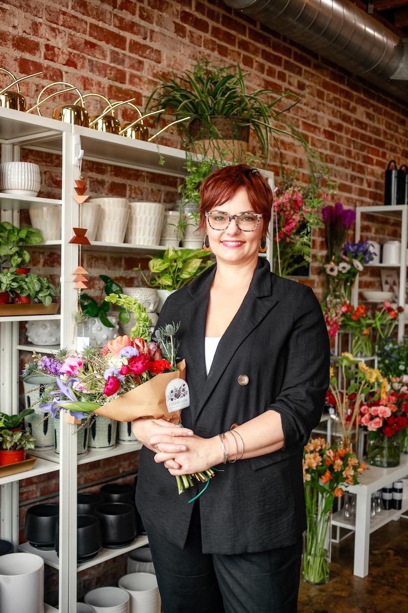 woman shop owner holding plant in front of shop display