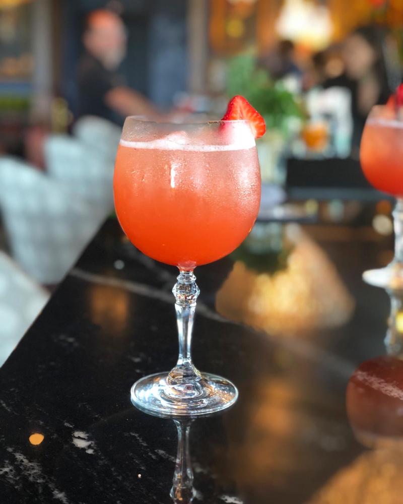 refreshing pink strawberry cocktail in globe glass sitting on a black marble bar