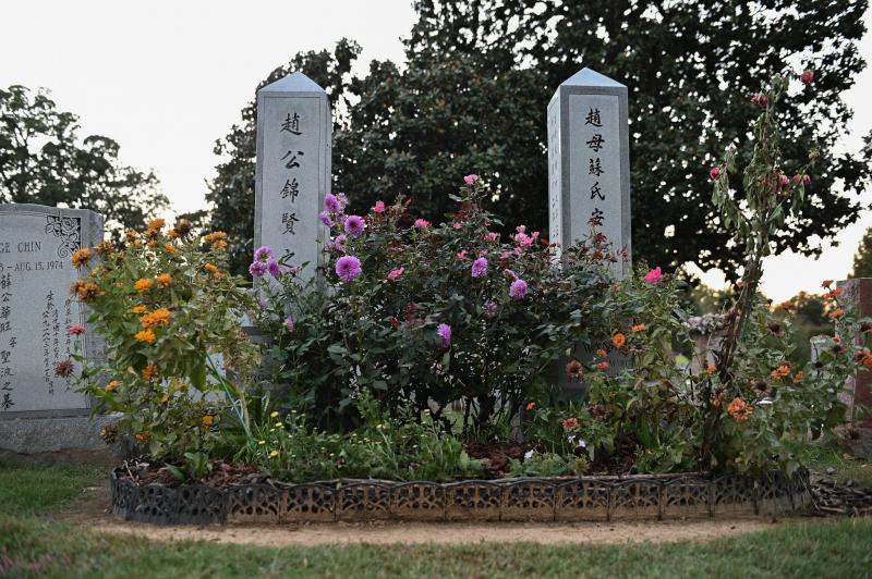 two small obelisks with Chinese characters surrounded by flowers at cemetery