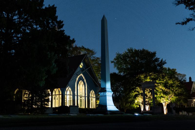 night photo of Gothic style chapel and large obelisk monument at cemetery