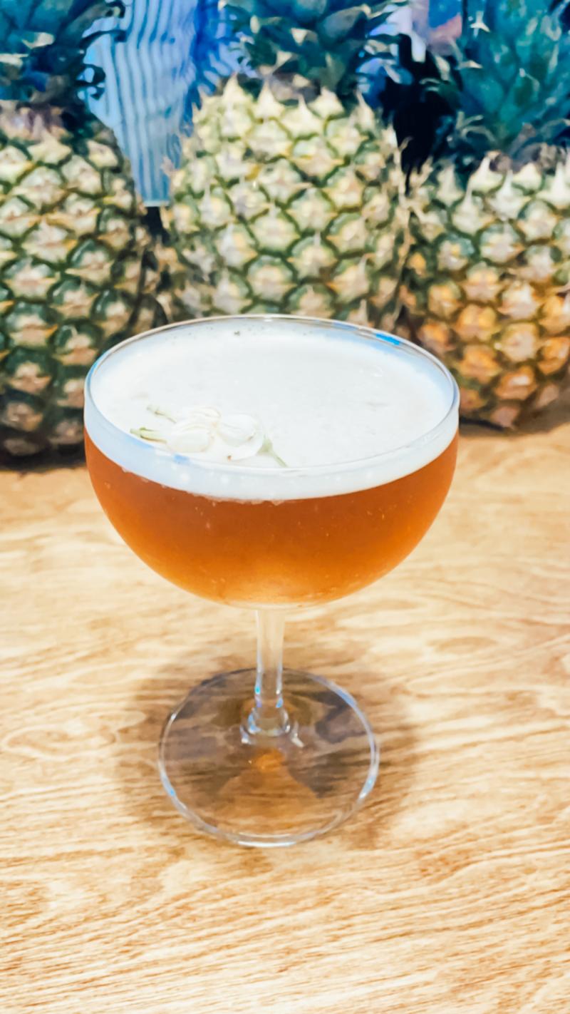 light brown cocktail with foam on top in coupe glass with pineapples
