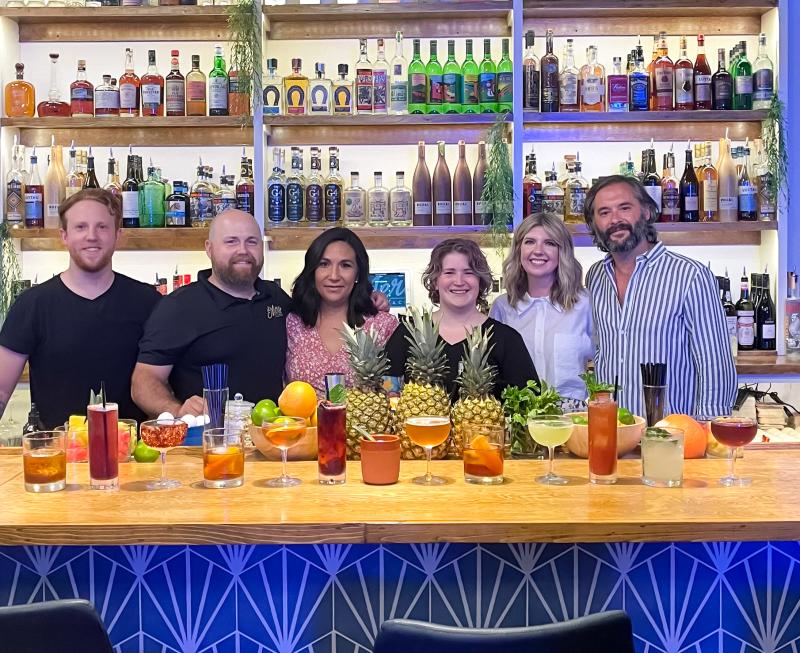 staff standing behind bar with a bunch of cocktails