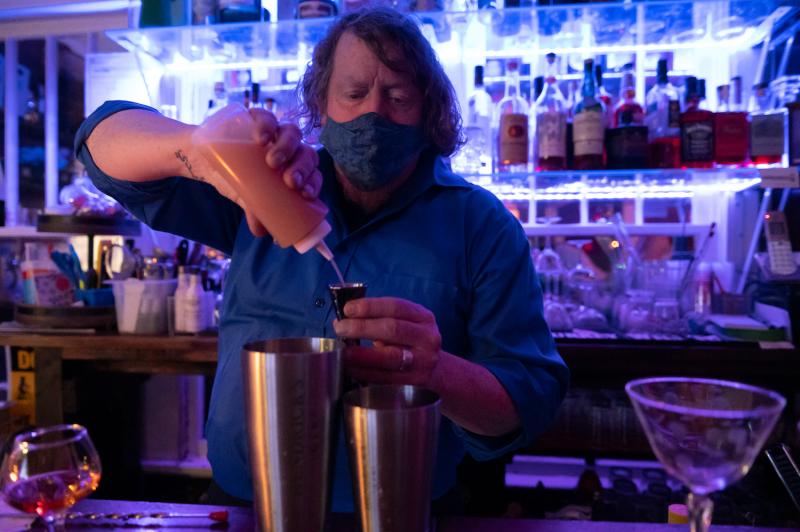masked bartender pour drink with blue lit bar in the background