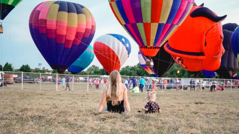 hot air balloon festival mom and kid sitting in a field