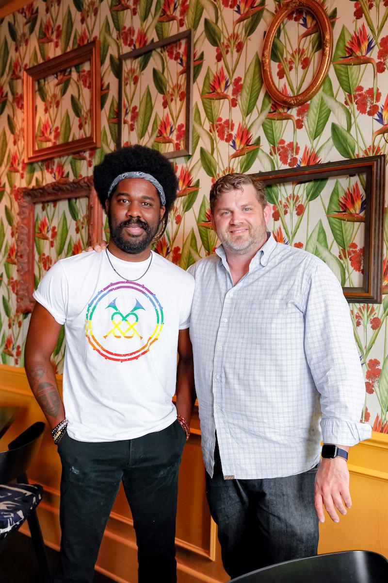 two men standing in a restaurant with floral wallpaper
