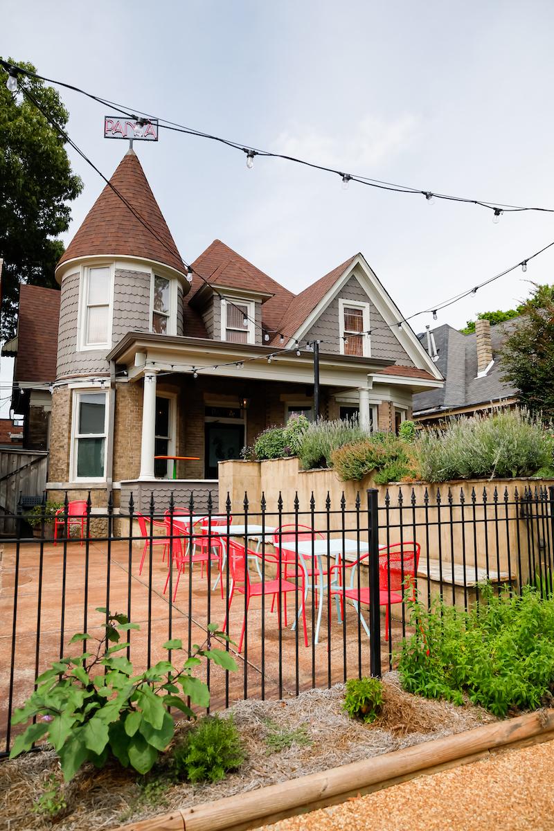 gray house with turrets that's been turned into a restaurant, shrubs all around, patio with red furniture out front