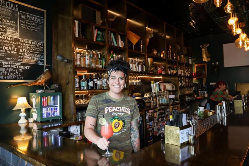 bartender in casual bar holding a pinkish colored drink in a wine glass